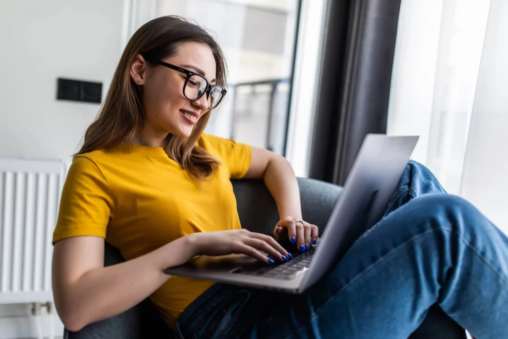 pessoa sentada em uma poltrona, notebook apoiado nas pernas e acessando a internet através de um serviço de provedor de internet
