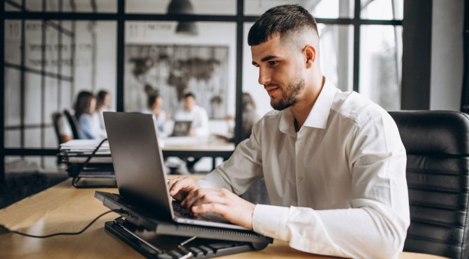 Homem sentado em cadeira, utilizando notebook e entendendo o que é link dedicado para provedor