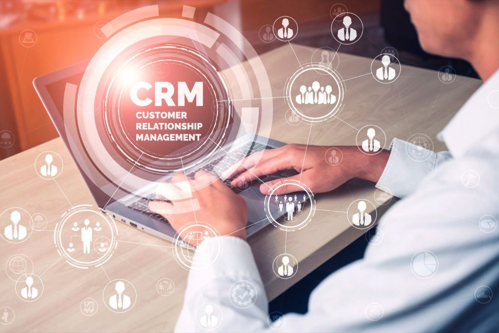 Homem usando um notebook ao fundo com ícone digital de CRM sobreposto à imagem.