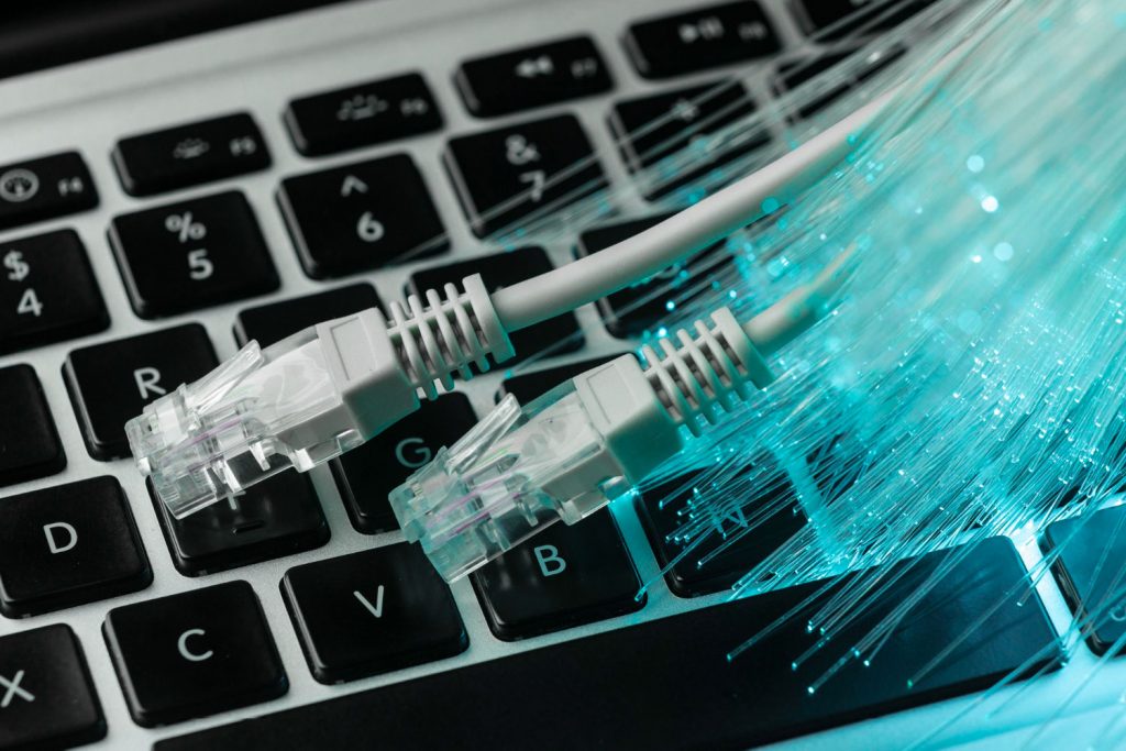 Cabo de fibra óptica sobre um teclado de notebook e filamentos luminosos representando o interior do cabo.