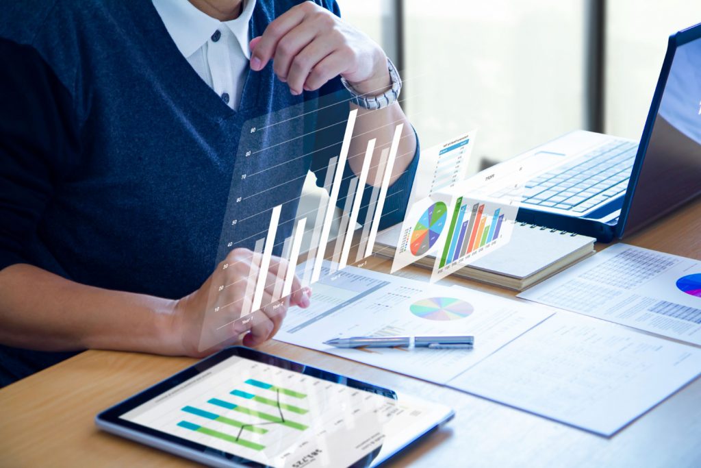 Homem fazendo gestão de provedores de internet e analisando gráficos em uma mesa com ícones de gráficos digitais na imagem.