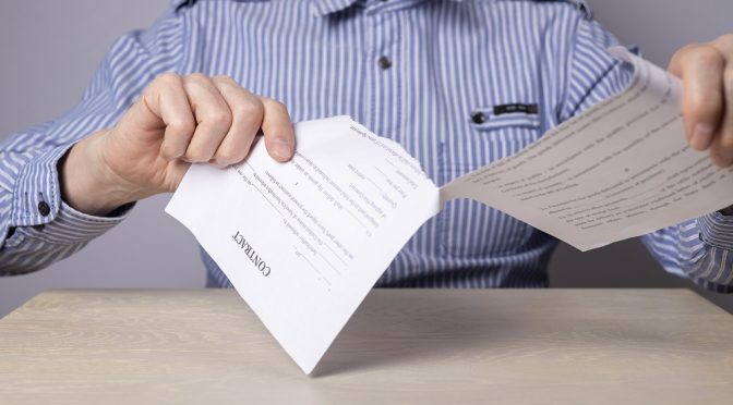cancelamentos-no-provedor Pessoa sentada em frente a uma mesa rasgando um contrato, representando os cancelamentos no provedor