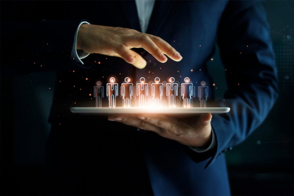 Pessoa segurando tablet e em cima ícones digitais de bonecos que estão sendo geridos pela outra mão, representando como organizar uma empresa.