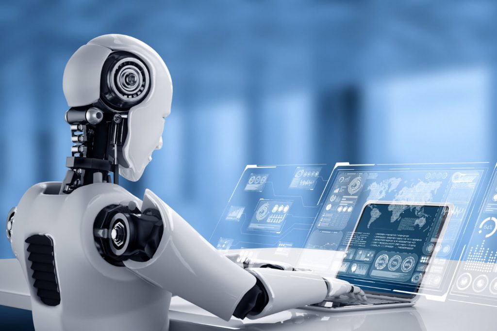 Robô humanóide sentado em frente a um notebook.