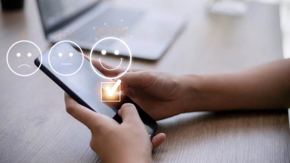 Pessoa no celular dando check em emoji feliz com 3 estrelas, representando pesquisa de satisfação do ISP