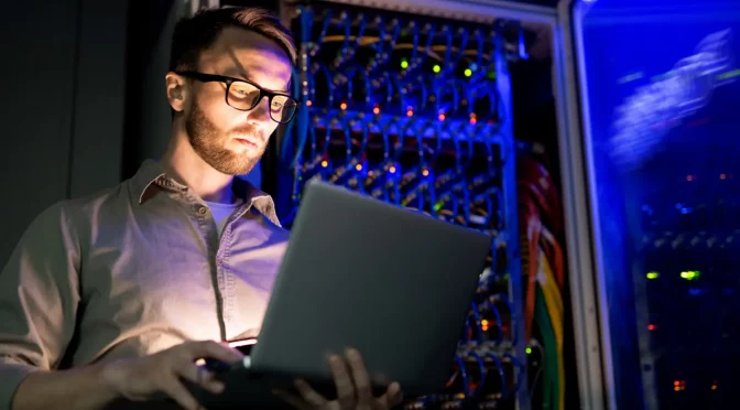 Homem analisando os equipamentos do provedor pelo notebook, evitando o desperdício de recursos no provedor de internet.