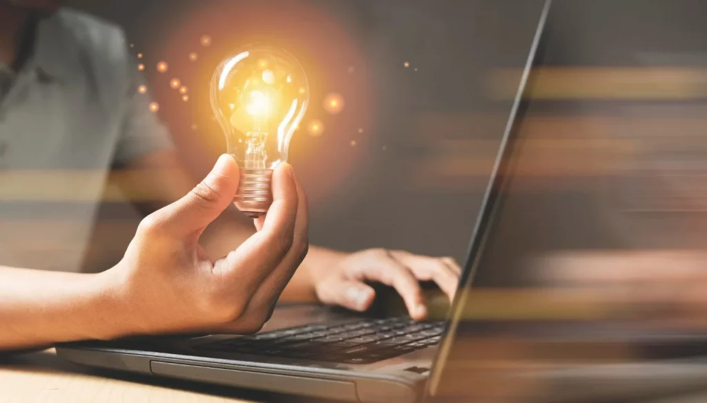 Homem com notebook e segurando lâmpada acesa, representando ideias para vender planos de internet fibra óptica.