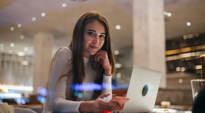 Mulher sorrindo utilizando um computador e um celular representando o cabo low friction